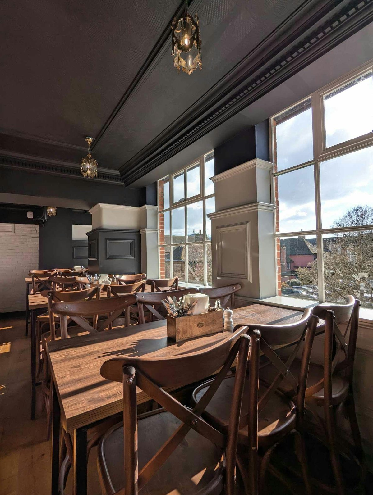 Two sets of wooden tables and chairs, in the window, with sunlight streaming in.